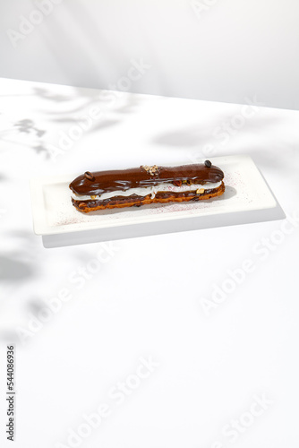 Chocolate eclair on white plate. French dessert stuffed custard cream. Eclair with coffee flavours Chocolate dessert on restaurant plate. Cchocolate eclair on light background photo