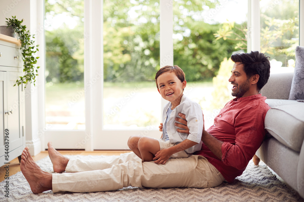 Father And Son At Home Sitting On Floor In Lounge Playing Game Together Father And Son At Home Sitting On Floor In Lounge Playing Game Together