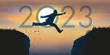Un homme saute par dessus un gouffre entre deux falaises devant un soleil au zénith et symbolise le passage à la nouvelle année 2023.