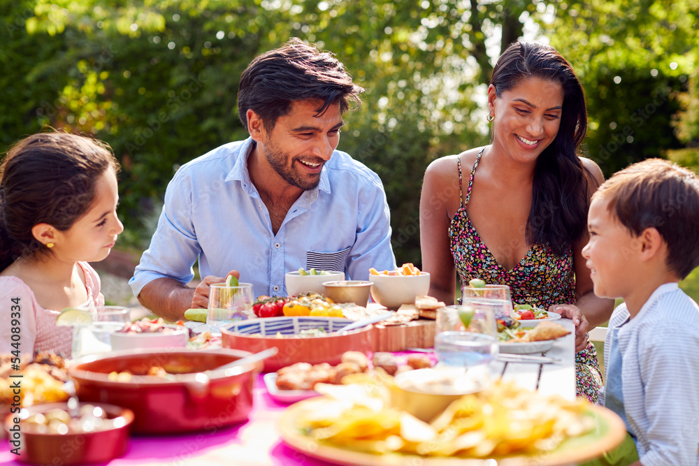 Family Eating Outdoor Meal In Garden At Home Together Family Eating Outdoor Meal In Garden At Home Together