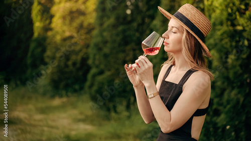 woman in a straw hat tastes or smells rose wine at a winery