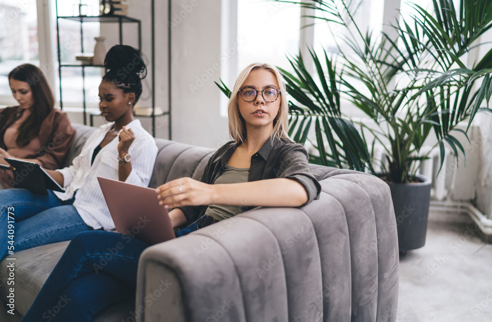 Pensive woman with laptop sitting on couch near colleagues