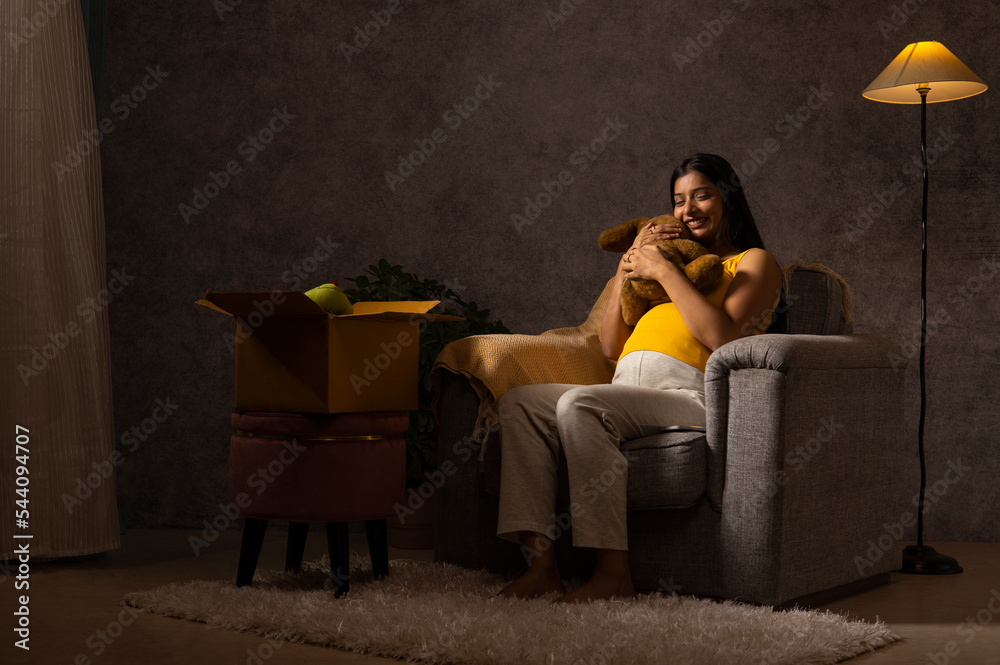 Naklejka premium Pregnant woman embracing toy while sitting on sofa at home