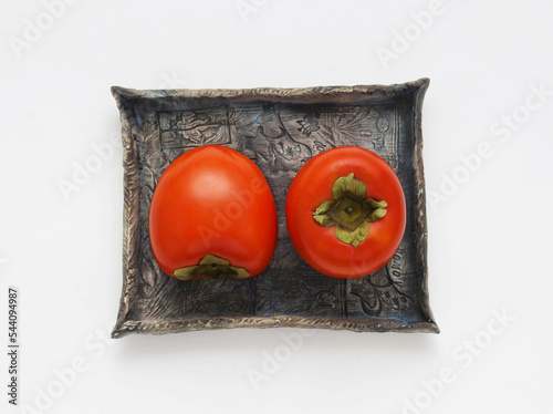 Persimmon fruits on a blue ceramic plate on a white background. Top view. Directly above photo.