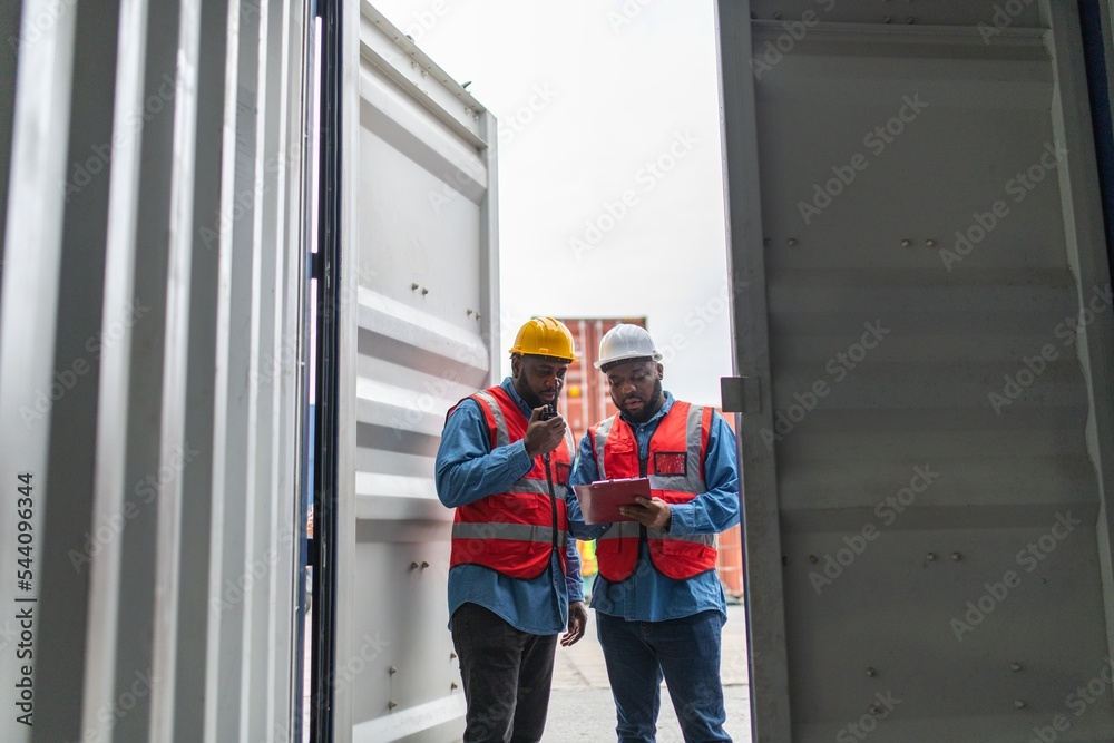 Two black african male professional engineers doing routine checkup on a container logistic shipping yard ensuring all containers are following procedure and safety regulation Two black african male professional engineers doing routine checkup on a container logistic shipping yard ensuring all containers are following procedure and safety regulation