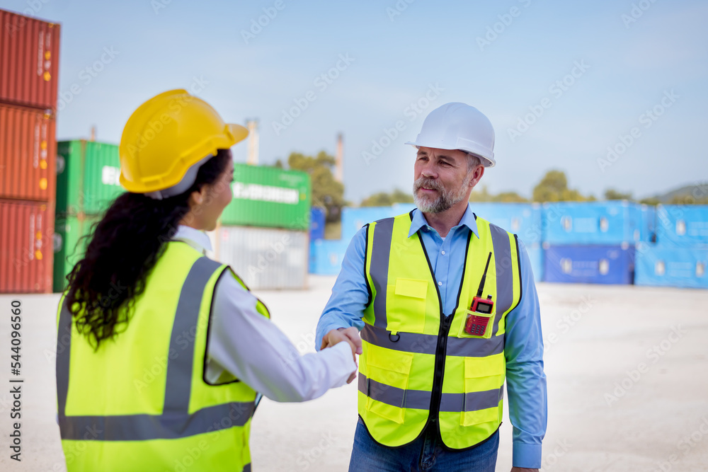 Engineers wearing safe uniform working in the construction container dock yard shaking hands together while standing by shipping containers in freight yard show good cooperation and teamwork concept. Engineers wearing safe uniform working in the construction container dock yard shaking hands together while standing by shipping containers in freight yard show good cooperation and teamwork concept.
