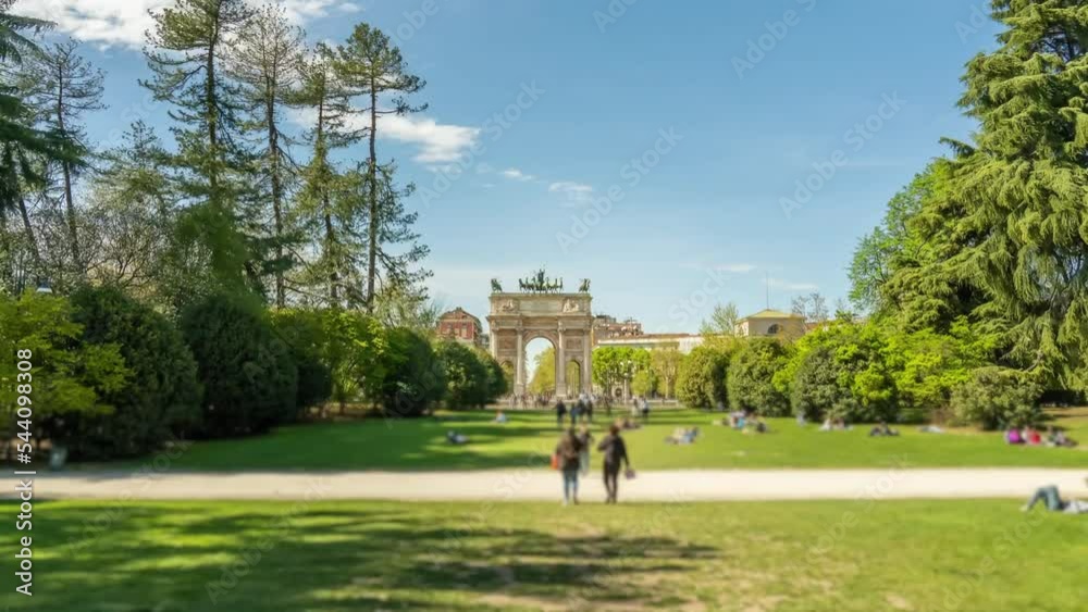 Triumphal Arch of Peace in city park with tourist crowd among trees on green grass lawns. Popular tourist destination in Milan on sunny day hyper lapse