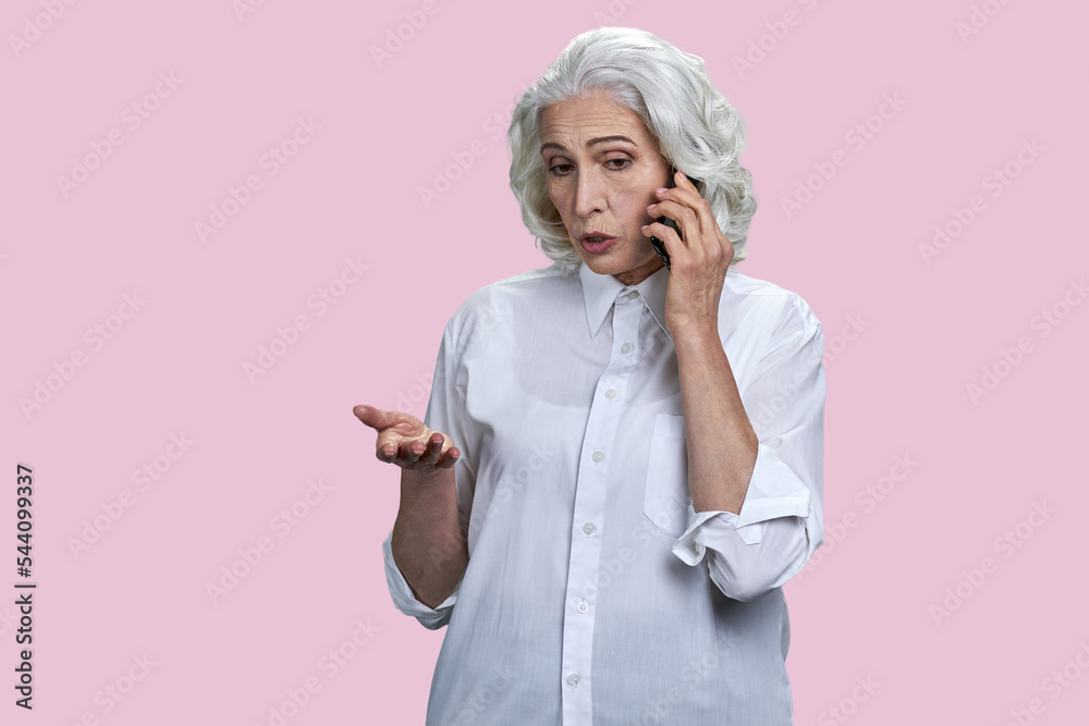 Portrait of senior gray-haired woman talking on phone. Isolated on pink background. Portrait of senior gray-haired woman talking on phone. Isolated on pink background.