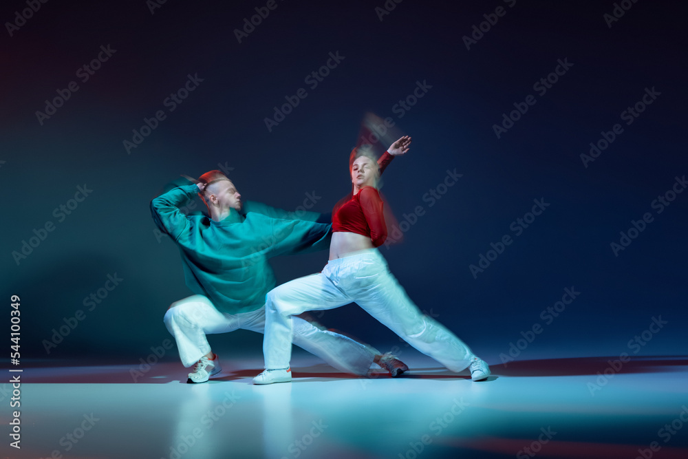 Portrait of young man and woman dancing with expression isolated over dark blue background with mixed lights