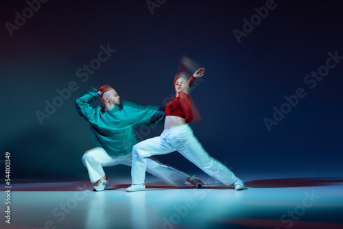 Portrait of young man and woman dancing with expression isolated over dark blue background with mixed lights