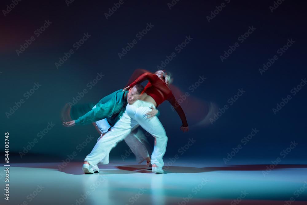 Portrait of young man and woman dancing isolated over dark blue background with mixed lights. Emotional dance