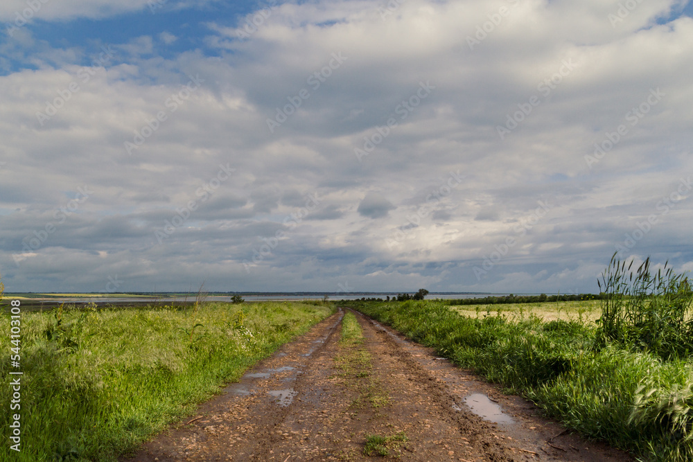 Rural path in field landscape photo. Beautiful nature scenery photography with waterside on background. Idyllic scene. High quality picture for wallpaper, travel blog, magazine, article Rural path in field landscape photo. Beautiful nature scenery photography with waterside on background. Idyllic scene. High quality picture for wallpaper, travel blog, magazine, article