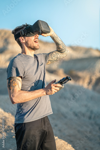 Young adult man looking amazed through virtual Reality fpv mask while flying drone in arid outdoors area.