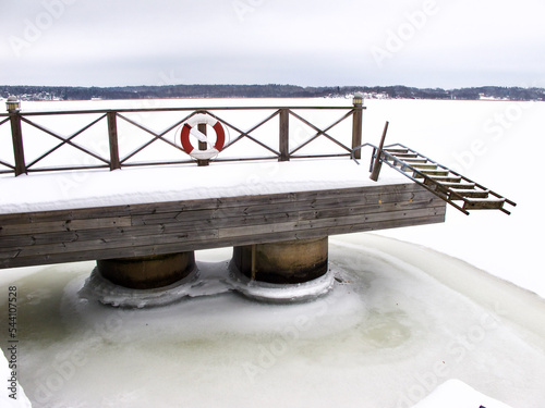 Pier with ladder in foggy winter landscape with snow and a frozen sea. photo