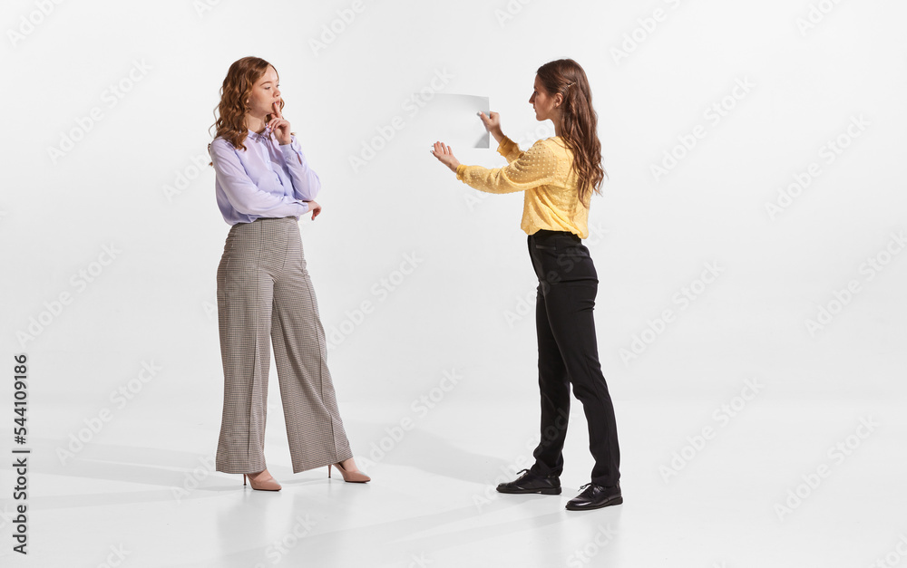 Naklejka premium Portrait of two women, employees working together, discussing business analytics isolated over white background