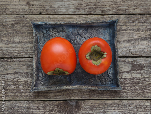 Persimmon fruits on a blue ceramic tray on a wooden background. Top view. Photo directly from above.