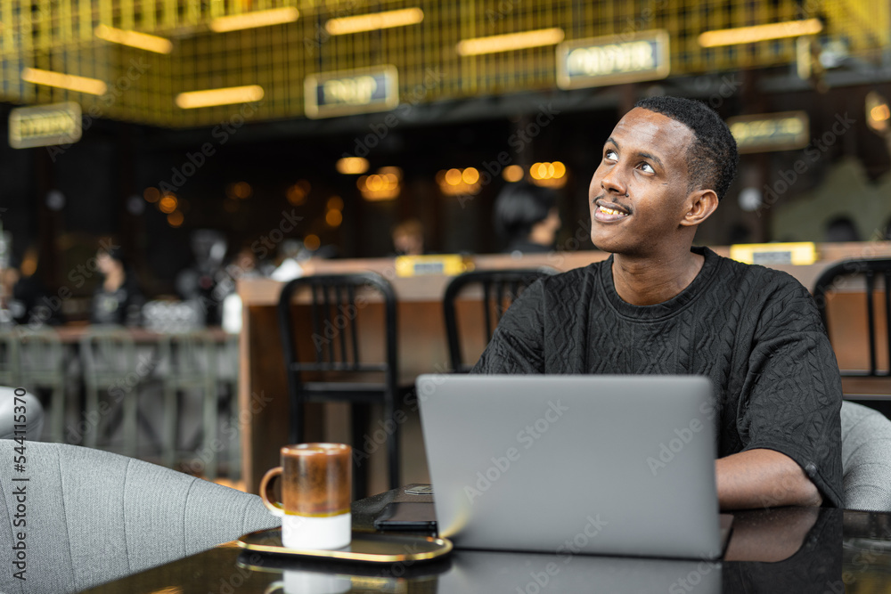 Obraz premium Portrait of handsome young African man using laptop computer in coffee shop