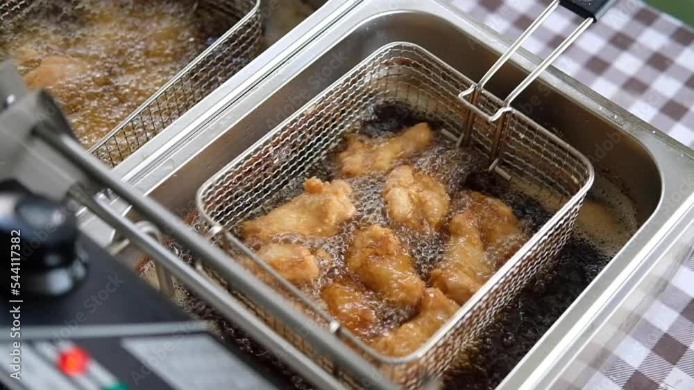 Frying chicken in deep fryer with bubbles of the oil are boiling while frying.