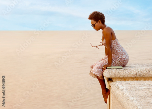 Black woman with afro and sunglasses thinking on the beach alone on a sunny day