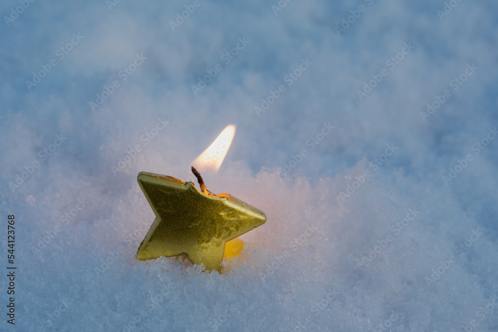 In the snow is a single burning candle in the form of a star. Evening. There is a small light around the candle. New year and christmas concept In the snow is a single burning candle in the form of a star. Evening. There is a small light around the candle. New year and christmas concept