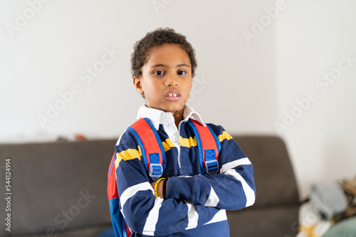 Ritratto in vita di un giovane afroamericano che guarda la fotocamera con le braccia incrociate mentre indossa lo zaino in casa. photo
