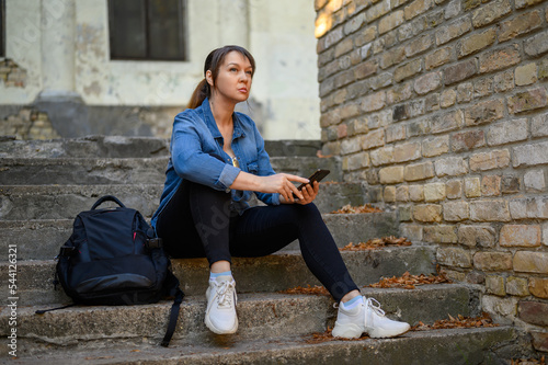 stylish woman sits on the stairs in a public park and holds a smartphone in her hands. © Marina Gordejeva