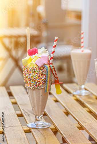 Fotografia Two freak shakes with marshmallow, meringue and marmalade on a wooden table in a cafe