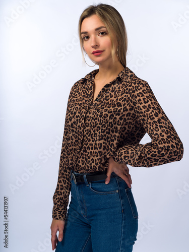 A beautiful, young, slender girl with long blonde hair on a white background in blue jeans and a stylish blouse with leopard spots. Close-up