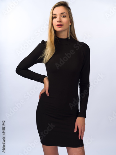 A beautiful, young, slender girl with long blonde hair on a white background in a short black dress that fits her figure. Close-up