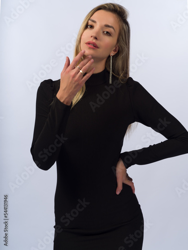 A beautiful, young, slender girl with long blonde hair on a white background in a short black dress that fits her figure. Close-up