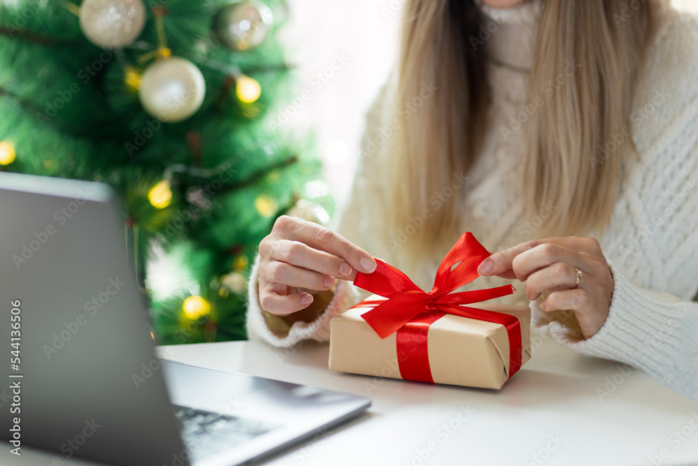 Young woman opening Christmas or new year present when calling to friends via video chat from home Young woman opening Christmas or new year present when calling to friends via video chat from home