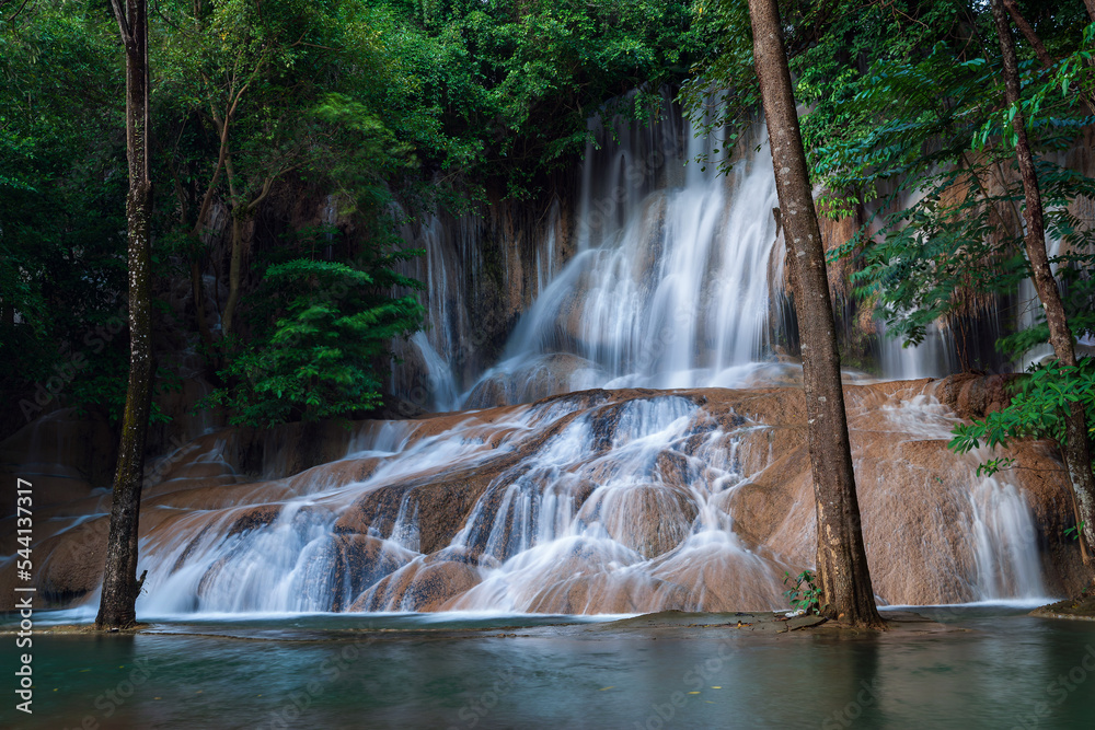 Obraz premium Shot from iconic Sai yok noi waterfall that flows through rock crevices down to a large emerald pool with green forest in Sai yok national park, Thailand.
