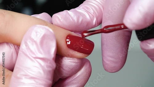 Master applies red gel polish on the nails, makes a manicure photo