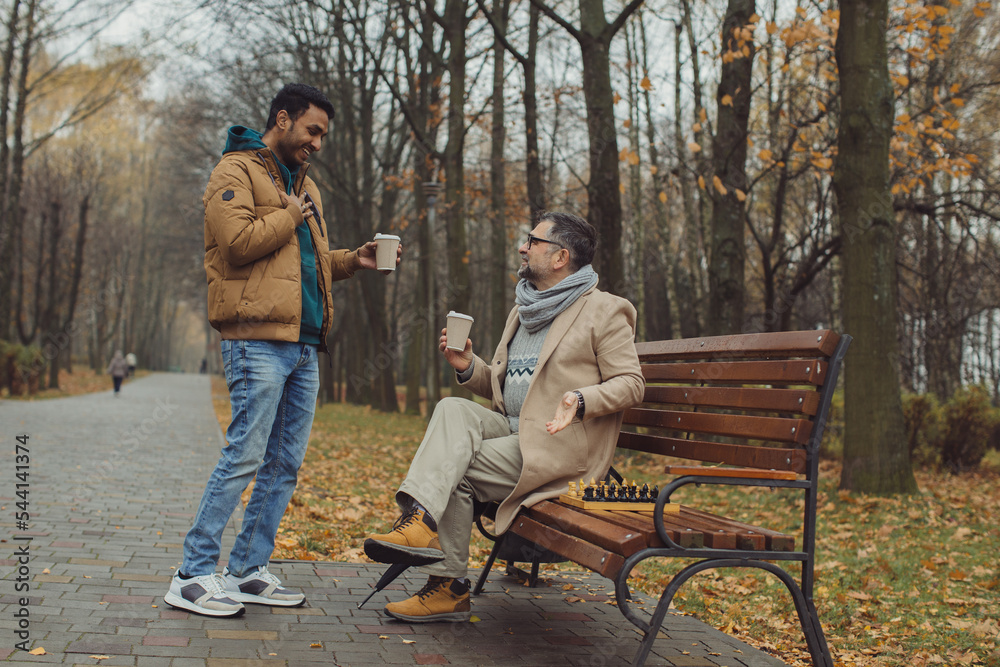 Multicultural friendship of people of different ages. A meeting of two friends for a game of chess in the park. Multicultural friendship of people of different ages. A meeting of two friends for a game of chess in the park.