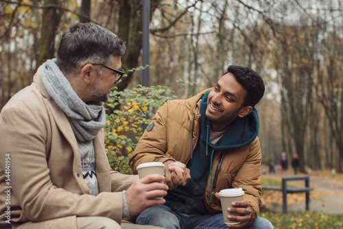 Smiling multiethnic men talking on bench in autumn park © dsheremeta