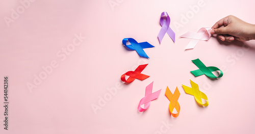 Fotografie Hand holding pink ribbon which is among colorful ribbons on pink background, can