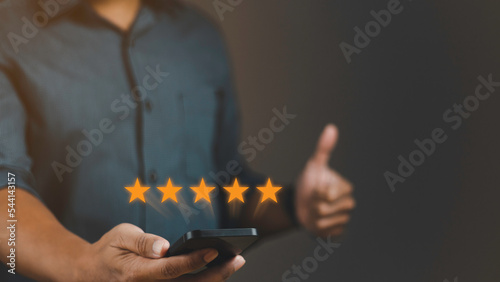 Customer review satisfaction feedback survey concept. User give rating to service experience on online application. Man using smartphone with five stars and showing thumbs-up.