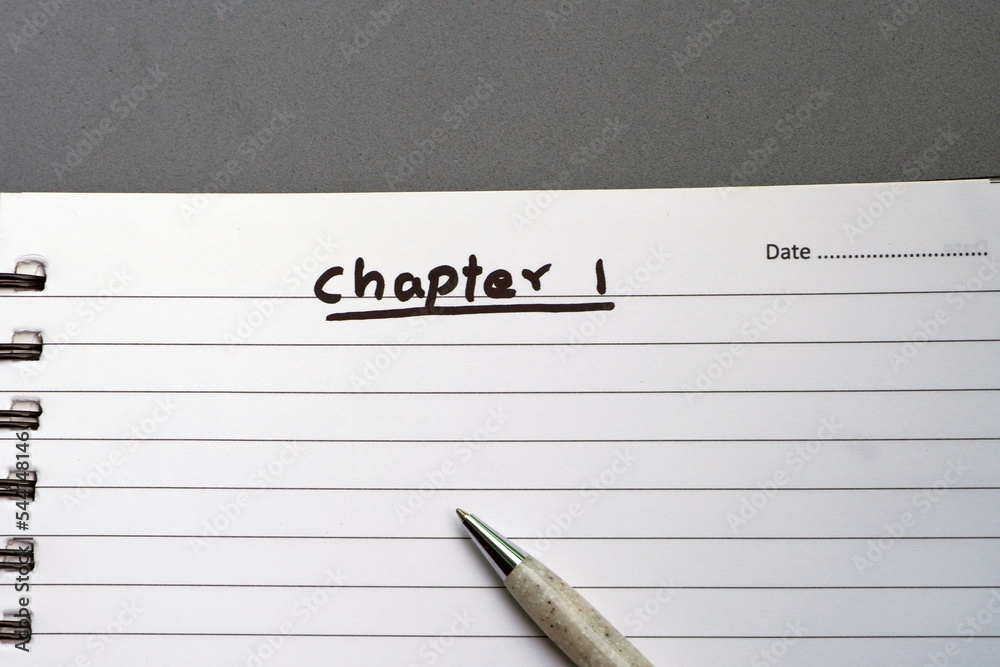 White notebook with text CHAPTER 1 written and a pen lying in the empty paper. First page of a diary or notebook to start for writing the content in book. White notebook with text CHAPTER 1 written and a pen lying in the empty paper. First page of a diary or notebook to start for writing the content in book.