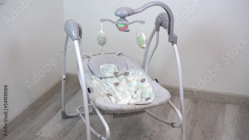 An empty swing-cradle swings in the room. Children's automatic swing for an infant.