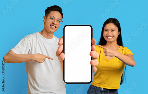 Nice Offer. Young asian couple holding and pointing at big blank smartphone © Prostock-studio