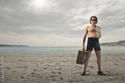satisfied man in bathing suit with suitcase and sunscreen at the beach photo