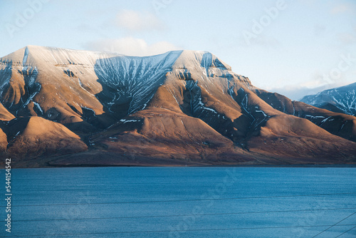 A snowy mountain in front of the town of Longyearbyen, the largest settlement and the center of Svalbard, Norway during a clear sunny day with blue sea