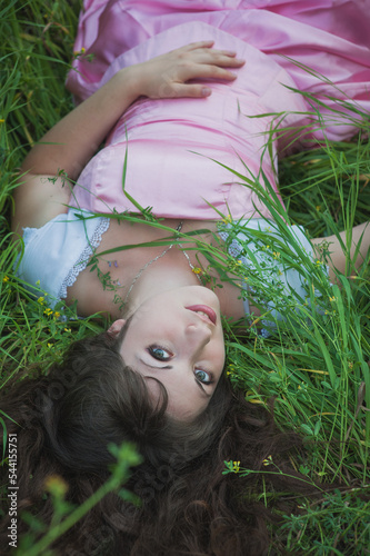 Beautiful woman with long hair and pink dress medieval style lying down in the grass