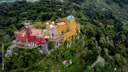 Cinematic aerial perspective of Pena Palace, Sintra, Portugal. Situated in top of a hill in the Sintra Mountains, surrounded by forest. In background Cintra city. Drone backward photo