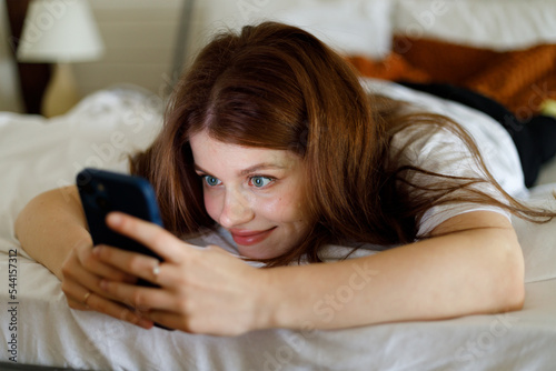 Social networks in bed. A young woman with a smartphone in her hands reads news on the phone, addiction to social networks.