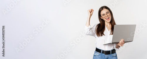 Enthusiastic office woman, businesswoman holding laptop and shouting with joy, celebrating and rejoicing, standing over white background