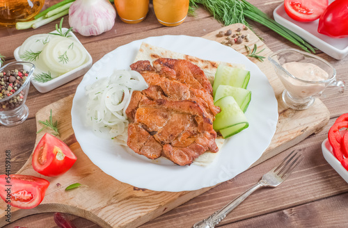 Pork meat skewers with onions and fresh vegetables on a white plate on a dark wooden background