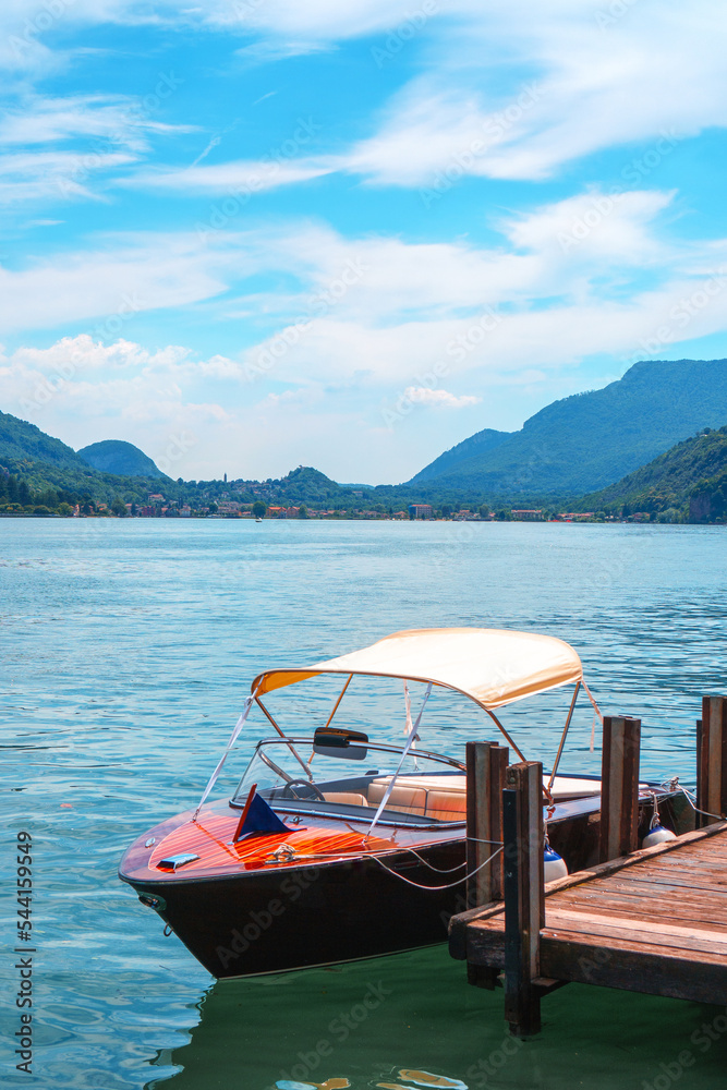 Splendid view of Lake Lugano with the luxury speedboat moored at the shore of Morcote in Switzerland. Beautiful Swiss landscape of the lake and Alps in the background on a sunny summer day.