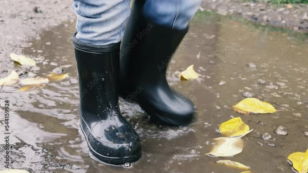 child in rubber boots stomps in a puddle, mud splashes. slow motion video child in rubber boots stomps in a puddle, mud splashes. slow motion video