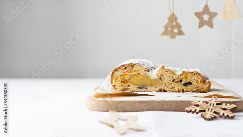 Traditional Christmas baking concept. Classic stollen with dried fruits, nuts and marzipan, sprinkled with powdered sugar on a cutting board on a white table. New year banner, background copy space.